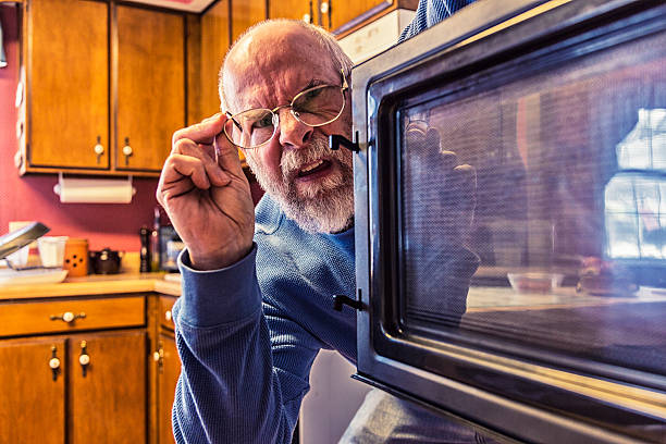 Senior Man Looking Into Kitchen Microwave Oven stock photo