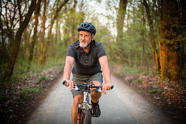 Senior man on his mountain bike outdoors Senior man on his mountain bike outdoors in forest on a lovely summer day, staying active cycling stock pictures, royalty-free photos & images