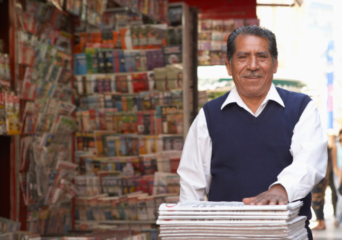 Senior man on newspaper  stand in street, smiling, portrait