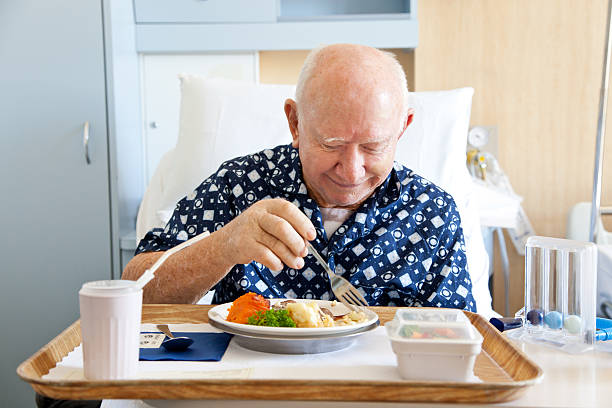 Senior Man Patient in Hospital Bed Eating Meal stock photo