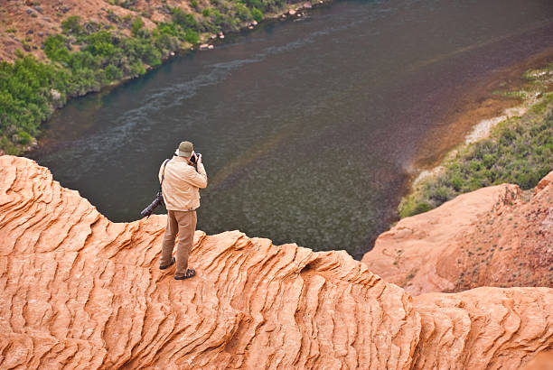 Senior Man Photographing the View of Horseshoe Bend Page, Arizona, USA - May 09, 2011: The Colorado River provides some incredible natural vistas along its length. One of the more unusual vistas is at Horseshoe Bend. The name was inspired by its unusual shape, a horseshoe-shaped meander of the river. Horseshoe Bend, located about four miles southwest of Page, Arizona, USA within the Glen Canyon National Recreation Area has become a very popular tourist attraction. In this picture, a senior man is standing on the steep cliff overlooking the river. jeff goulden southwest usa stock pictures, royalty-free photos & images