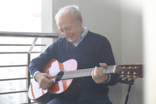 senior mann spielt gitarre auf einem balkon - 60 69 jahre stock-fotos und bilder
