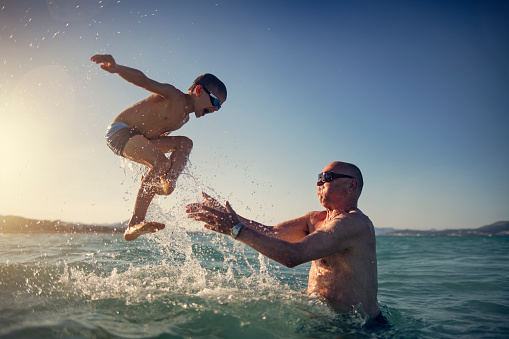 Little boy playing with his grandfather in the sea. The grandfather is tossing the happy boy into the sea. Sunny summer day.
Nikon D850