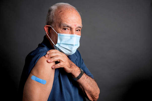 Senior man posing showing his vaccination band-aid in his arm stock photo