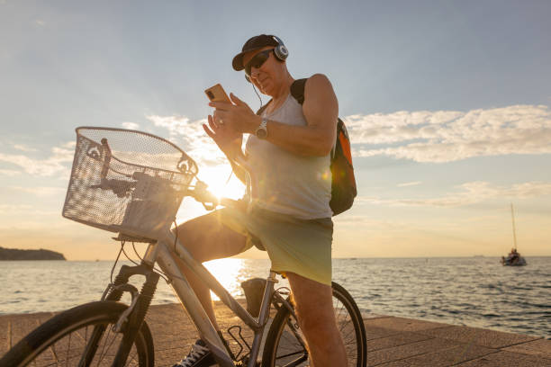 senior man riding a bike and listening the music - senior listening music beach bildbanksfoton och bilder