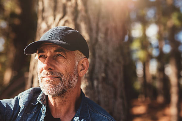 Senior man sitting in woods on a summer day Close up portrait of senior man wearing cap looking away. Mature man with beard sitting in woods on a summer day. looking away stock pictures, royalty-free photos & images