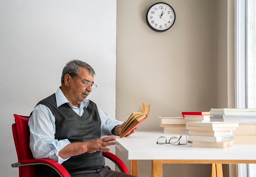 Senior man stays at home in quarantine reading book during coronavirus pandemic