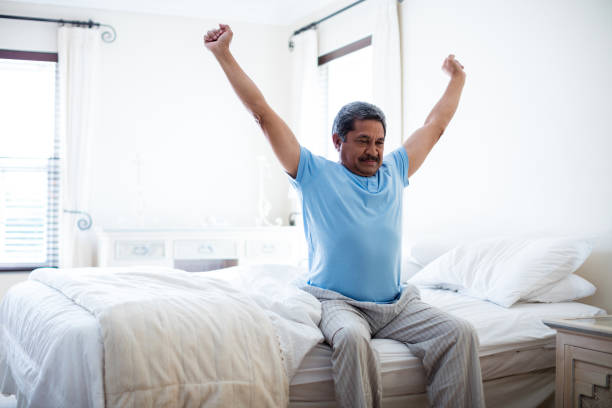 Senior hombre estirando los brazos en la cama en dormitorio - foto de stock