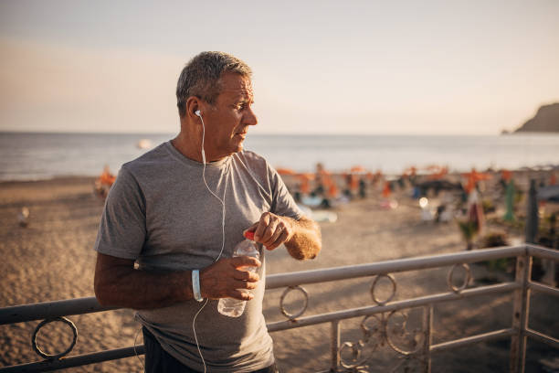 senior man taking a water break after jogging - senior listening music beach bildbanksfoton och bilder