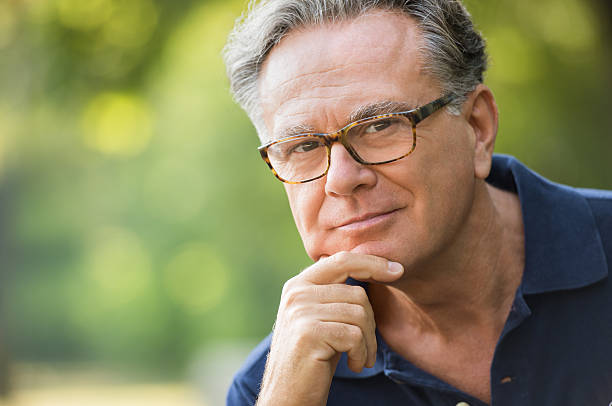 Senior man thinking Close up face of satisfied senior man at park looking at camera. Portrait of mature man sitting in the park with hand on chin. Smiling old man in casual thinking outdoor. hand on chin stock pictures, royalty-free photos & images