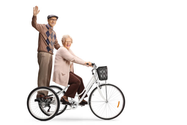 Senior man waving from a tricycle and senior woman riding Senior man waving from a tricycle and senior woman riding isolated on white background adult tricycle stock pictures, royalty-free photos & images