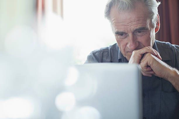 homem idoso com as mãos juntas usando computador portátil - preocupado imagens e fotografias de stock