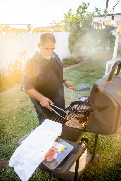 senior mexikanische mann grillen steaks am grill - fett verbrennen senior stock-fotos und bilder