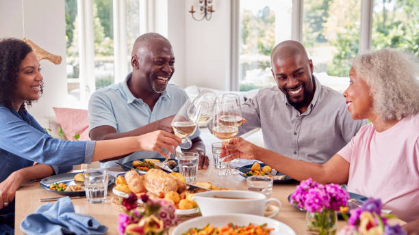 Senior Parents With Adult Offspring Making Toast Sitting Around Table For Family Meal stock photo