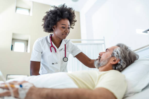 Senior patient on bed talking to African American female doctor in hospital room, Health care and insurance concept. Doctor comforting elderly patient in hospital bed or counsel diagnosis health. stock photo