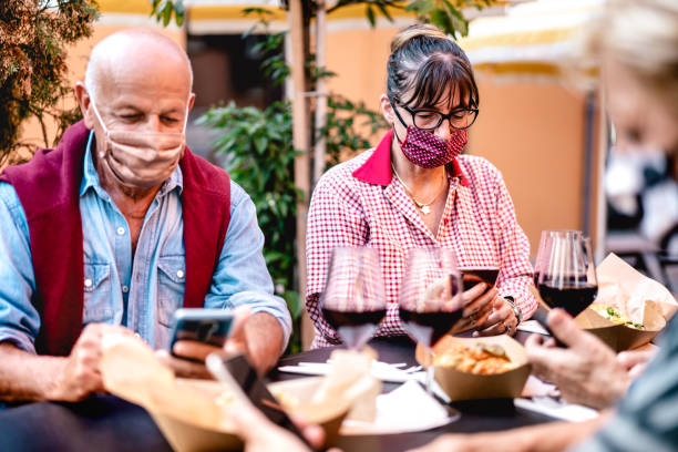 Senior people using mobile smart phone with face mask covered - Retired adults worried while watching news on smartphone - New normal lifestyle concept at restaurant wine bar - Vivid contrast filter Senior people using mobile smart phone with face mask covered - Retired adults worried while watching news on smartphone - New normal lifestyle concept at restaurant wine bar - Vivid contrast filter baby boomers restaurant stock pictures, royalty-free photos & images