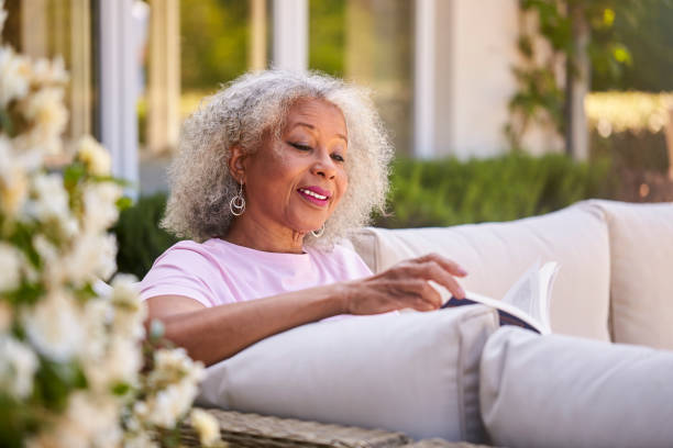 Senior Retired Woman Relaxing On Outdoor Seat At Home Reading Book stock photo