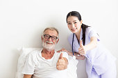 Senior retirement man and asian nurse show thumb up with smile  in a room