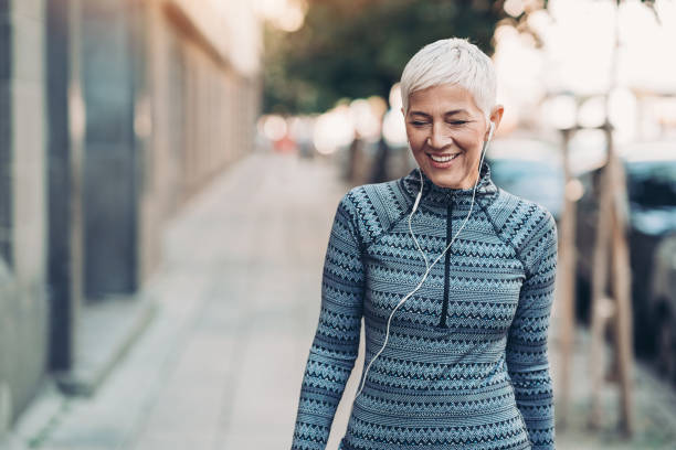 Senior sportswoman walking on the street Senior female athlete walking outdoors in the city 55 59 years stock pictures, royalty-free photos & images