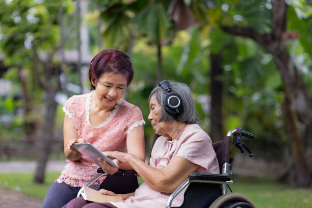 senior woman and daughter listening music with headphone in backyard stock photo