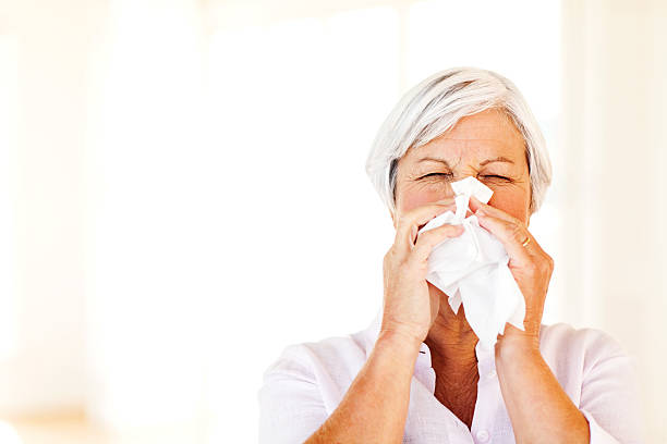 Senior Woman Blowing Nose With Tissue At Home stock photo