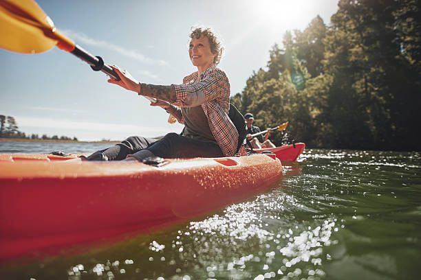 senior woman canoeing in lake on a summer day - kajak stockfoto's en -beelden