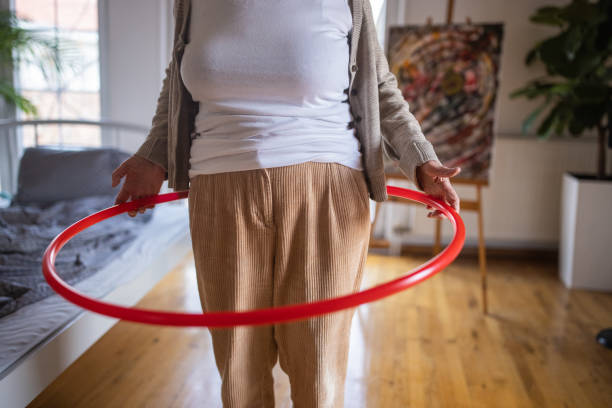 Senior woman having fun with plastic hoop in bedroom at home stock photo