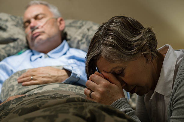 Senior woman kneeling prays over a sick man in bed stock photo