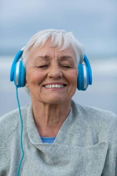 senior kvinna lyssna på musik i hörlurar - senior listening music beach bildbanksfoton och bilder