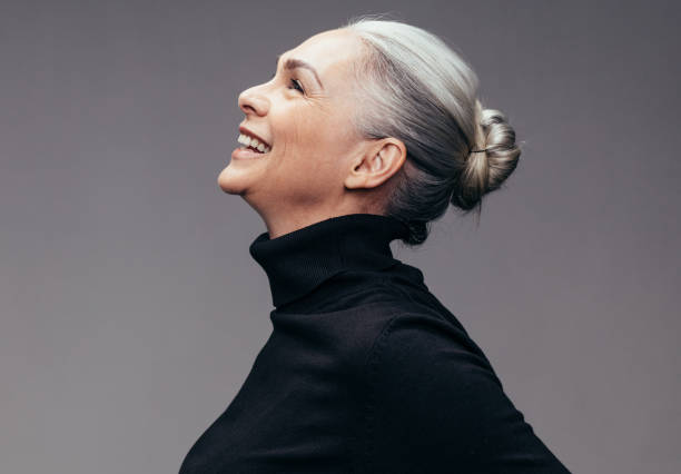 Senior woman looking happy Side view of senior woman laughing on gray background. Profile view of mature woman in black casuals looking happy older woman stock pictures, royalty-free photos & images