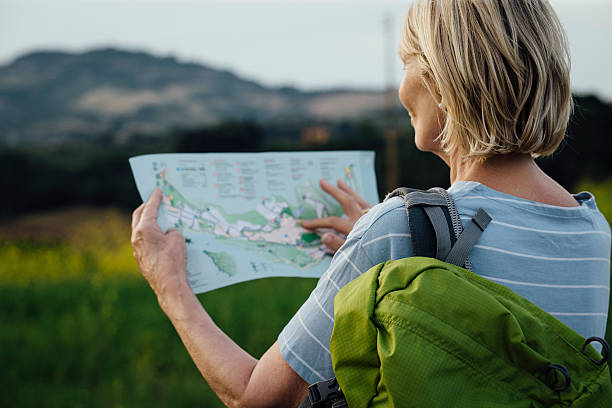 Senior Woman Outdoors with a Map and Backpack Rear view of a senior woman holding a map in the Italian countryside as she stands with a bag over her shoulder. Close up head and shoulders view. person looking at map stock pictures, royalty-free photos & images