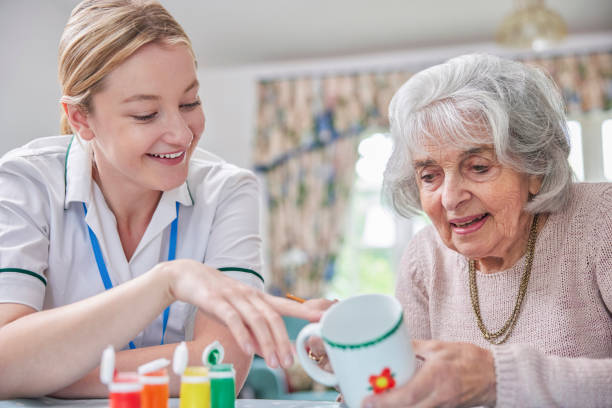 Senior Woman Painting Cup With Art Therapist stock photo