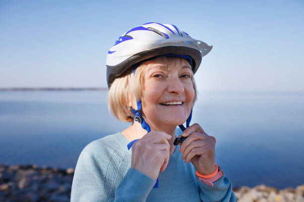 Senior woman puts on safety helmet before roller skating in nature, mental and physical health stock photo