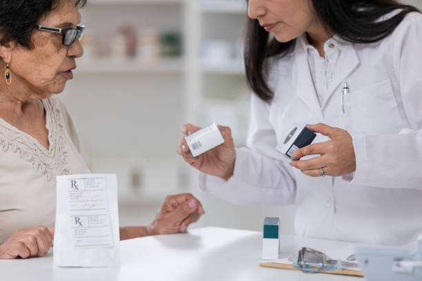 Senior woman receives multiple prescriptions at pharmacy Senior woman discusses medication with pharmacist. The pharmacist is filling several prescriptions for the woman. generic drug stock pictures, royalty-free photos & images