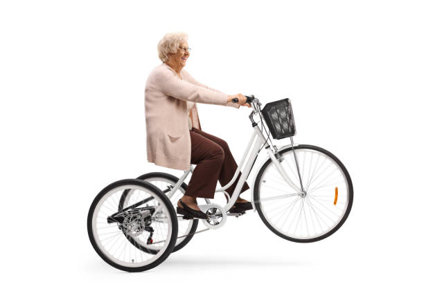 Senior woman riding a tricycle and lifting the front wheel Senior woman riding a tricycle and lifting the front wheel isolated on white background adult tricycle stock pictures, royalty-free photos & images
