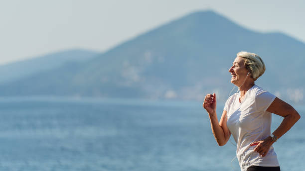 senior kvinna som springer på bakgrunden havet - senior listening music beach bildbanksfoton och bilder
