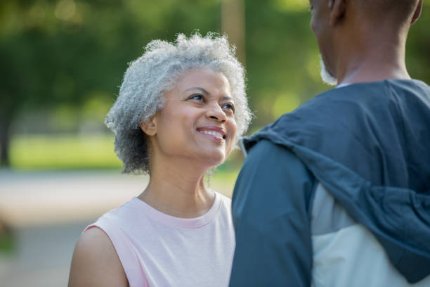 Senior woman smiles lovingly at husband while exercising Senior adult African American woman is smiling and looking lovingly at her husband while the couple exercises and walks in public park. old black couple in love stock pictures, royalty-free photos & images