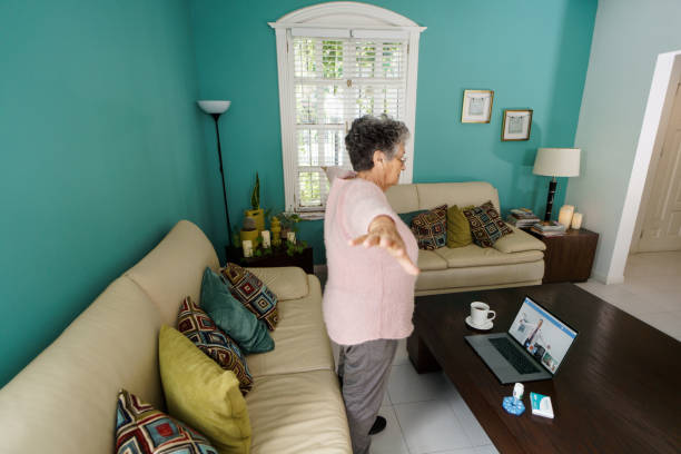 Senior woman standing and raising arms during remote consultation A latin senior woman standing and raising her arms at home during a remote consultation with a doctor. doctor of physio therapy online stock pictures, royalty-free photos & images
