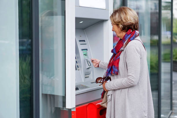 Senior woman using ATM in the city stock photo