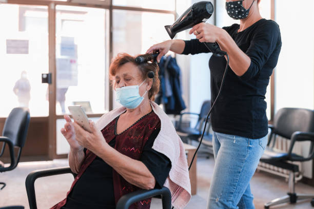 Senior woman using smart phone when at hair dresser's Older woman with protective mask using mobile phone at hair salon dry conditioner stock pictures, royalty-free photos & images