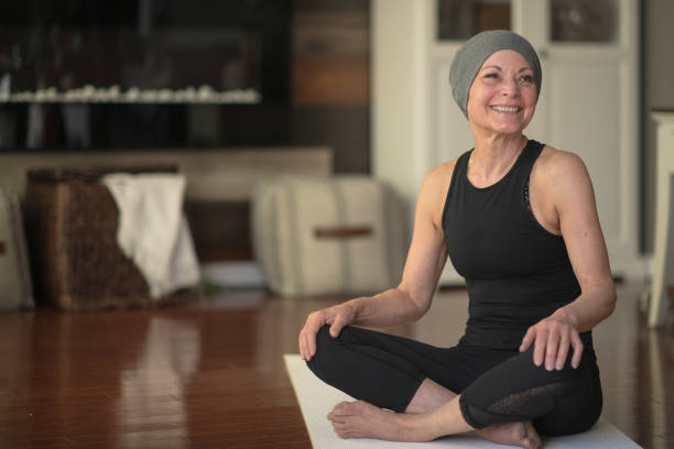 Senior woman with cancer A senior woman with cancer does yoga at home in her living room. She is wearing black active wear. survival stock pictures, royalty-free photos & images