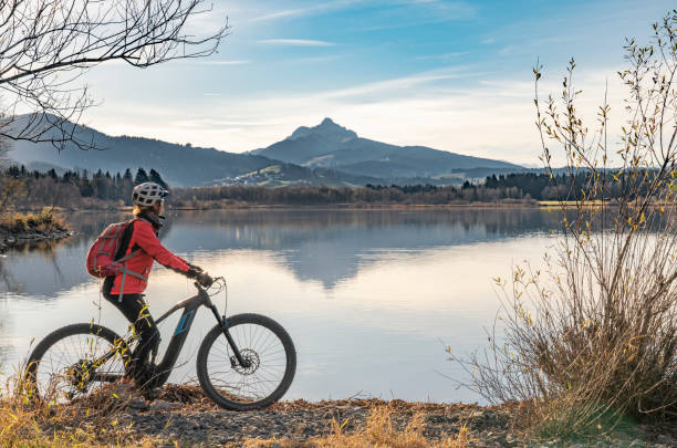 senior woman with electric mountain bike at lake Gruentensee, Allgau alps nice senior woman with electric mountain bike enjoying the view over lake autumnal Gruentensee in the Allgaeu alps near Nesselwang, Bavarian Alps, Germany allgau alps stock pictures, royalty-free photos & images