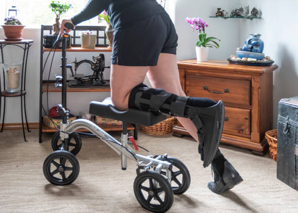 Senior Woman with Walking Boot on Knee Scooter In Bedroom stock photo