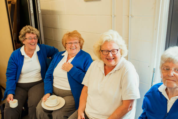 Four senior women sitting together indoors and having coffee. They...