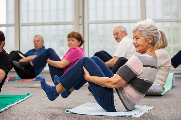 Group of senior adults sitting on the floor and doing stretching pilates exercises with raising their legs.