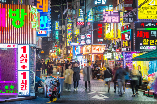 Crowds of people walking through the colourfully illuminated neon night streets of Sinchon, Seoul, South Korea.