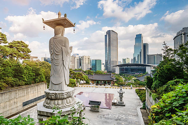 Famous Bongeunsa Temple Buddha Statue. Modern Skyscrspers of downtown Seoul in the background under blue summer sky. Half aerial view from the jungle behind the temple.  Bongeunsa is a buddhist temple located in Seoul, South Korea, Asia.