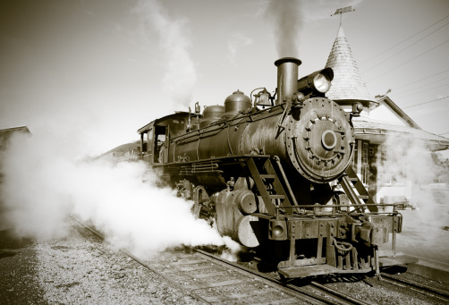 A sepia toned vintage steam locomotive begins it's journey from the station