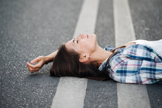 Serene woman lying on an asphalt road, looking up at the sky. Side view. stock photo