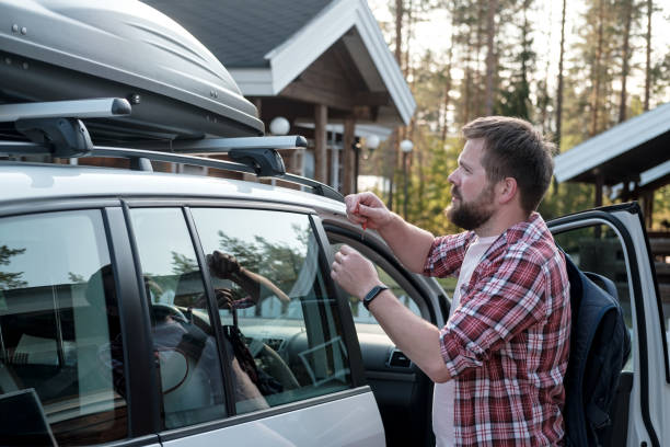 serious, bearded man with a backpack holds the keys in hand and is about to open the roof rack of the car. - fechar porta bagagens imagens e fotografias de stock